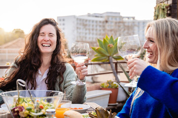 Happy friends celebrating cheering with wine outdoor in winter time at patio restaurant - Focus on left girl face