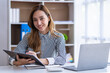 © crizzystudio - Portrait of a cheerful Asian businesswoman using a laptop and writing on a charger to keep notes as a base