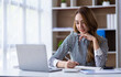 © crizzystudio - Portrait of a cheerful Asian businesswoman using a laptop and writing on a charger to keep notes as a base