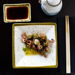 Tasty octopuses (Pulpitos) on square plate with herbs in restaurant