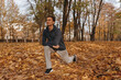 Fit male runner in sportswear doing lunge exercise and stretching legs while training in nature in autumn 