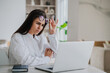 © Iona - Perplexed young Brunette Caucasian businesswoman in white shirt sits at desk with laptop takes off her glasses in disbelief looks at screen of computer with upset face expression. Business and finance