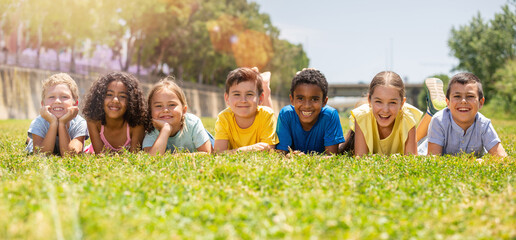 Wall Mural - Group of school children resting on grass and smiling together in park