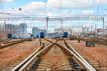 An Extensive Network Of Railway Tracks Against The Background Of A Blue Cloudy Sky And A Cityscape.