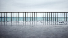 Low Angle View Of Raindrops On Concrete With Railing And Lake In Background