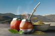 Calabashes with mate tea and bombilla on light grey table and beautiful view of mountain landscape