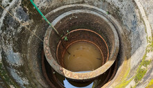 Undrinkable And Unhygienic Bad Muddy Contaminated Brown Or Yellow Color Dirty Drinking Water Inside Old African Damaged Well. Drought, Less Rainfall, Shortage, Scarcity And Crisis In Africa Concept.