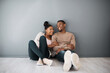 Homeowner, love and beginning with a black couple sitting together in their new home on a gray wall background. Real estate, room and mortgage with a man and woman on the floor after moving house
