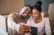 © T Hover/peopleimages.com - Phone, couple and selfie while moving in to home, real estate or apartment, happy and proud on a floor. New house, property and man with woman on a living floor for picture, moment and bonding