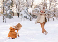 Two Happy Kids Throwing Snowballs At Each Other While Playing With Snow In Winter Park