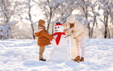 Sticker - Cute little boy making snowman with mom in winter park