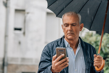 Canvas Print - middle aged man with umbrella and smartphone in the street