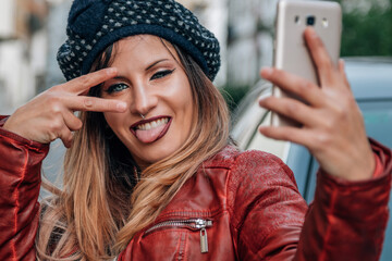 young woman making the peace symbol and sticking out her tongue while taking a photo with the phone