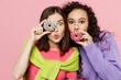 © ViDi Studio - Young two friends happy joyful fun women 20s wears green purple shirts together eat sweet donuts snack cover mouth eye look camera isolated on pastel plain light pink color background studio portrait.