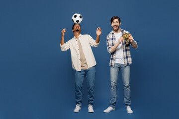 Full body young two fan friends men wear white casual shirts together cheer up support football sport team hold soccer ball on head cup watch tv live stream isolated plain dark royal blue background.