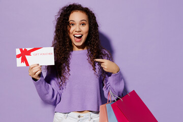 Young woman wear pullover hold paper package bags after shopping point on store gift certificate coupon voucher card isolated on plain pastel light purple background Black Friday sale buy day concept