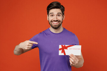 Poster - Young surprised happy brunet caucasian man 30s wear casual basic purple t-shirt hold point finger on gift certificate coupon voucher card for store isolated on plain orange background studio portrait.