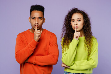 Wall Mural - Young secret couple two friend family man woman of African American ethnicity in casual clothes together say hush be quiet with finger on lips shhh gesture isolated on pastel plain purple background