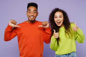 Young fun smiling couple two friends family man woman of African American ethnicity wear casual clothes together point finger on himself show thub up isolated on pastel plain light purple background.