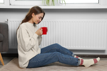 Poster - Woman holding cup with hot drink near heating radiator indoors