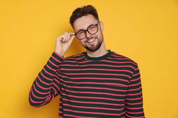 Wall Mural - Handsome man in striped sweatshirt and eyeglasses on yellow background