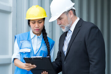 Male and female container yard workers discuss of container boxes from cargo freight ship at commercial dock site. Container boxes transportation or delivery goods concept