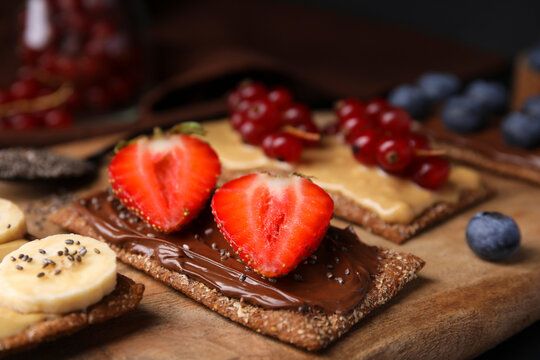 Fresh crunchy rye crispbreads with different toppings on wooden board, closeup