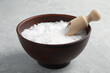 Natural sea salt in wooden bowl and scoop on light grey marble table