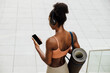 © Drobot Dean - Young fit sporty afro woman with yoga mat holding phone