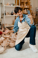 Wall Mural - Smiling mature woman making videocall and gesturing while sitting at workshop