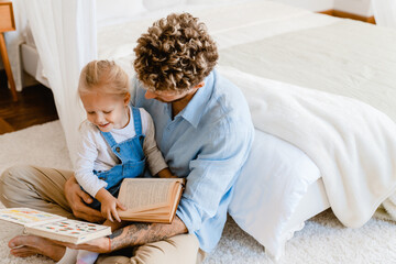 Young father and his little daughter reading books together at home