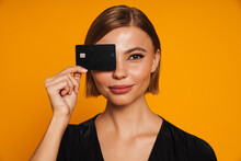 Young Smiling Woman Covering Her Eye With Credit Card Isolated Over Orange Background