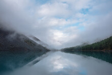 Tranquil Meditative Misty Scenery Of Glacial Lake With Reflection Of Pointy Fir Tops And Clouds At Early Morning. Graphic EQ Of Spruce Silhouettes On Calm Alpine Lake Horizon. Mountain Lake In Fog.