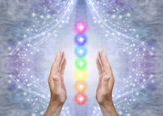 Canvas Print - Sensing Seven Chakras and Sending Healing - Male parallel hands with 7 rainbow coloured energy centres between against a blue flowing sparkling background and copy space 
