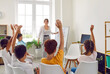 © Studio Romantic - Selective focus on raising hands in college classroom. Education in small groups. Interior of class room with large windows and blackboard for felt-tip pens. Young happy professor.