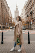 Concept of Poland lifestyle and travel towns in Warsaw. Young beautiful woman walking with bouguet of tulips on Warsaw city. Woman have a beautiful bouquet of yellow tulips standing outdoors in city.