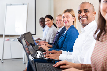 Wall Mural - Side view of cheerful hispanic businessman working on laptop with group of colleagues during corporate seminar