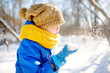 Little boy blowing snow from his hands. Child enjoy walking in the park on snowy day. Baby having fun during snowfall. Outdoor winter activities for kids.