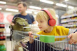 © Maria Sbytova - Cute preschooler boy with headphone and player is sitting in a shopping cart at a food store or supermarket. A child is listening to music or an audiobook while his parents buying groceries.