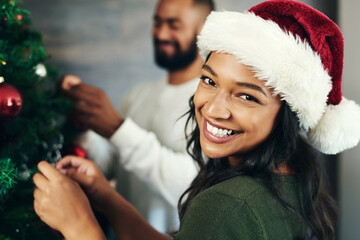 Couple, portrait and christmas tree decor together with love and care during the festive season. Husband, wife and hanging ornaments on an xmas tree while decorating with tinsel and bauble