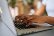 © dikushin - Close-up side view of unrecognizable African-American business woman typing on laptop keyboard sitting at home office desk, on beautiful blurry background.