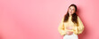 © Mix and Match Studio - Young smiling woman touching her stomach with relieved, happy face, feeling good after eating yoghurt or medicine from painful cramps, standing against pink background