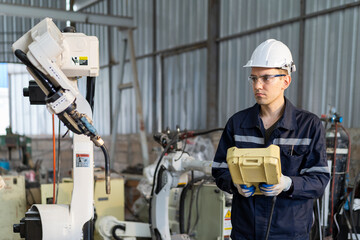 Wall Mural - Male engineer using robot controller working with adept robot arm in workshop. Male technician working with control automatic robot arm system welding. Industry robot manufacturing technology