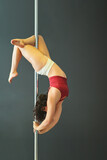 Young woman in red top and white panties performing acrobatics on a pole dance in a rehearsal room. 