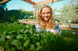 © StratfordProductions - Happy young caucasian woman in checked shirt looking at camera by plants in plant nursery