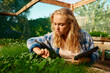 © StratfordProductions - Young caucasian woman holding digital tablet while picking plants in plant nursery