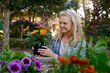 © StratfordProductions - Happy young caucasian woman holding potted flowers and smiling in garden center