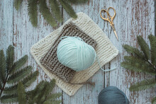 Overhead view of a ball of wool on crochet squares on a table with fir branches and a pair of scissors