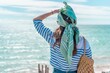 Woman with a green headscarf covering her eyes from the sun and enjoying the scenic seascape view