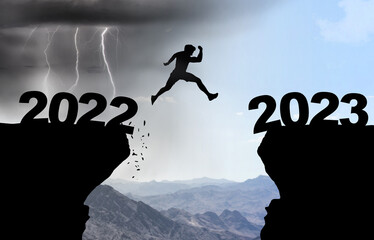 Man jumps over abyss with thunderstorm in background and inscription 2022 and 2023